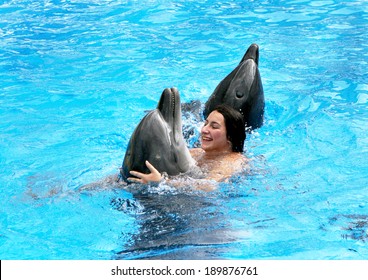 Happy beautiful young girl laughs and swims with dolphins in blue swimming pool on a clear sunny day