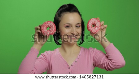 Happy beautiful young girl on a chroma key background having fun with donuts. Cute woman in a pink shirt posing with donuts. Making faces
