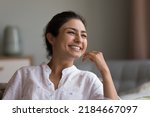 Happy beautiful young Indian woman looking at window with toothy smile, thinking of future vision, good news, dreaming, touching chin, facial skin, laughing. Head shot portrait