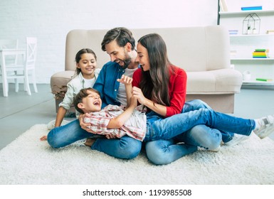 Happy Beautiful Young Parents Are Smiling, Hugging And Playing With Them Kids At Home Together