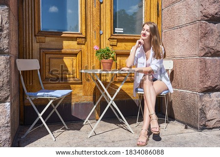                                Happy and beautiful young white woman is sitting outdoor in sunlight in white t-shirt ande taking sun.