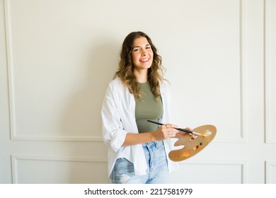 Happy Beautiful Young Woman Artist Using A Palette To Start Painting A Wall Mural 