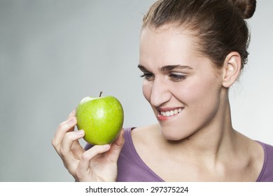 happy beautiful young woman biting lips to resist in eating appetizing green apple for symbol of beauty and healthy nutrition