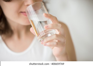 Счастливая красивая молодая женщина питьевая вода. Улыбающаяся кавказская женская модель держит прозрачное стекло в руке. Крупный план. Фокус на руке