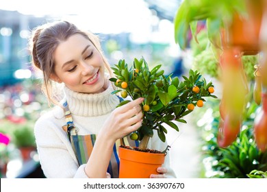 Happy beautiful young woman gardener holding small mandarine tree in orange pot in greenhouse Stock Photo