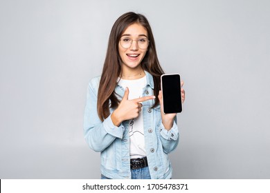 Happy beautiful young woman with long curly hair holding blank screen mobile phone and pointing finger over white background
