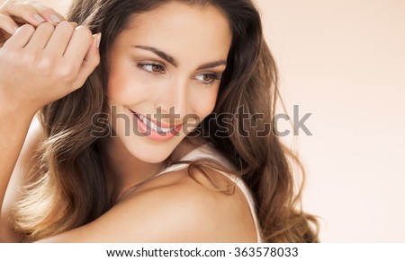 Happy beautiful young woman with long hair smiling over beige background. Fashion and beauty concept in studio. 