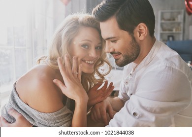 So happy! Beautiful young woman showing her engagement ring and smiling while sitting in the bedroom with her boyfriend