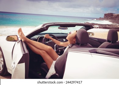 Happy Beautiful Young Woman Sitting In A Sports Car On Beautiful Sunny Summer Day. Sexy Woman's Legs Showing Out Of The Car, Enjoying Freedom Feeling Happy On The Hawaiian Beach. 