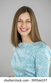 Happy beautiful young woman in a turquoise dress on a gray background. Studio portrait