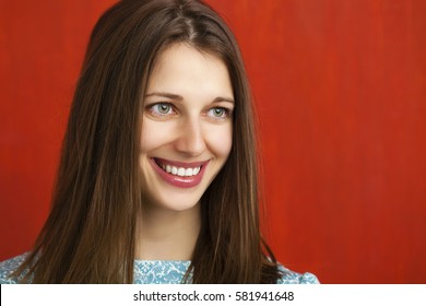 Happy beautiful young woman in a turquoise dress on red background. Studio portrait