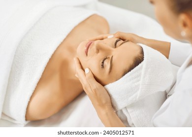 Happy beautiful young woman with white towel turban on head relaxing and enjoying facial treatment done by professional beautician at spa salon. Skin care, beauty procedures, face massage concept - Powered by Shutterstock