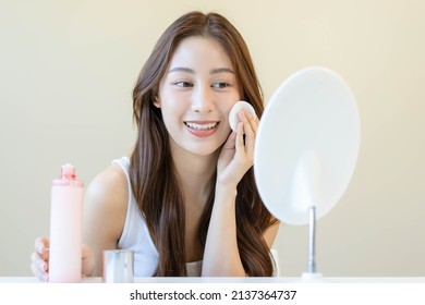 Happy beauty, beautiful asian young woman, girl looking in to mirror, holding cotton pad, applying facial wipe on her face, removing makeup before shower in bathroom, skin care on white background. - Shutterstock ID 2137364737