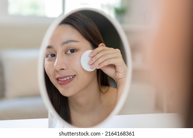 Happy Beauty, Beautiful Asian Young Woman, Girl Smiling, Looking In Mirror, Holding Cotton Pad, Applying Lotion By Wipe On Her Face, Removing Makeup Before Shower At Home. Skin Care Routine People.