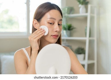 Happy Beauty, Beautiful Asian Young Woman, Girl Smiling, Looking In Mirror, Holding Cotton Pad, Applying Lotion By Wipe On Her Face, Removing Makeup Before Shower At Home. Skin Care Routine People.