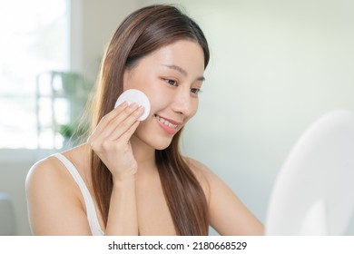 Happy Beauty, Beautiful Asian Young Woman, Girl Smiling, Looking In Mirror, Holding Cotton Pad, Applying Lotion By Wipe On Her Face, Removing Makeup Before Shower At Home. Skin Care Routine People.