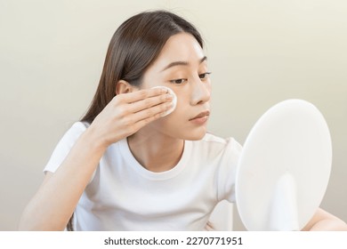 Happy beauty, beautiful asian young woman, girl looking in to mirror, holding cotton pad, applying facial wipe on her face, removing makeup before shower in bathroom, skin care on white background. - Powered by Shutterstock