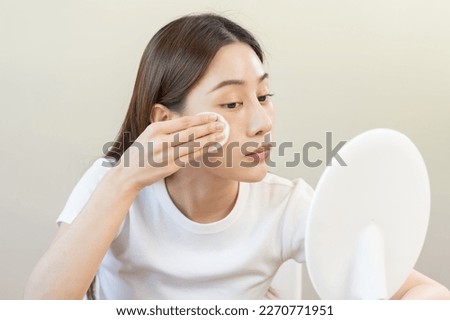 Happy beauty, beautiful asian young woman, girl looking in to mirror, holding cotton pad, applying facial wipe on her face, removing makeup before shower in bathroom, skin care on white background.