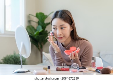 Happy Beauty Blogger Concept, Pretty Asian Young Woman, Girl Make Up Face By Applying Pink Blush By Brush On Cheek, Looking At The Mirror On Table At Home. Female Look With Natural Fashion Style.