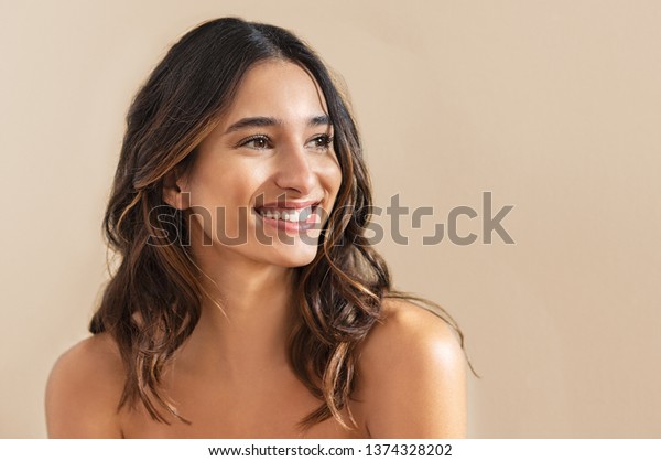 Happy beauty woman\
looking away isolated on background. Cheerful young brunette with\
nude shoulder smiling after skin treatment. Beautiful hispanic girl\
waiting spa therapy.