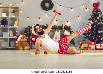 Happy Beginner Athlete In Funny Underwear And Santa Hat Made New Year Resolution To Keep Fit And Healthy And Is Doing Supine Side Leg Raises With Dumbbells During Home Workout On Christmas Holidays