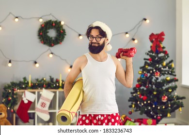 Happy Beginner Athlete In Funny Underwear And Santa Hat Made New Year Resolution To Keep Fit And Healthy And Is Doing Supine Side Leg Raises With Dumbbells During Home Workout On Christmas Holidays