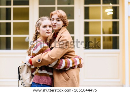 Happy best friends embracing. Sad girl crying and her sisiter comforting embracing her in front of the school building outdoor. Outcast, lonely, isolation, relation, social, concept.