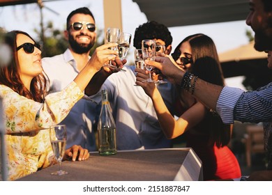 Happy best friends at terrace party toasting with Prosecco white wine in a summer afternoon - young people clinking flutes and having fun - trendy people carefree in the weekend at rooftop party