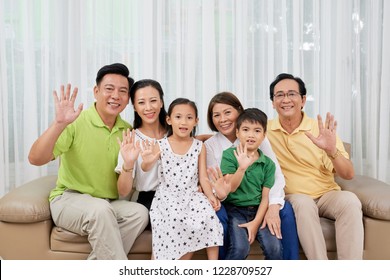 Happy Big Asian Family Sitting On Sofa And Waving At Camera