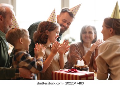 Happy Big Beautiful Family In Party Hats Clapping Hands And Smiling While Celebrating Little Girls Birthday At Home, Cute Child Feeling Excited After Blown Out Candles On Cake And Receiving Presents