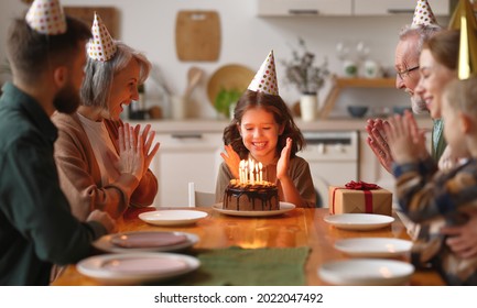 Happy big beautiful family in party hats clapping hands and smiling while celebrating little girls birthday at home, cute child feeling excited during  blown out candles on cake and receiving presents - Powered by Shutterstock