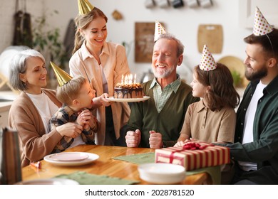 Fröhliche große, kaukasische Familie, die Partyhüte trägt, die Großväter zum Geburtstag im Haus feiern, glücklicher älterer Mann Großvater, der Kuchen mit hellen Kerzen hält, der Glückwunsch während der Feier zu Hause