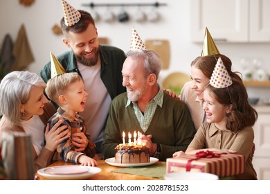 Happy Big Caucasian Family Wearing Party Hats Celebrating Grandfathers Birthday Indoors, Happy Elderly Man Grandpa Holding Cake With Lit Candles, Receiving Congratulationg During Celebration At Home