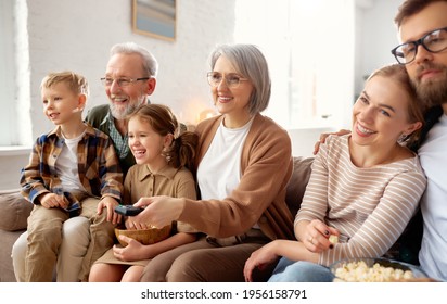 Happy Big Family Enjoying Weekend Together At Home. Grandparents, Mother, Father And Two Little Kids, Sister And Brother, Sitting On Coach And Eating Popcorn While Watching Funny Movie Comedy On TV