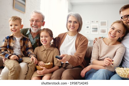 Happy Big Family Enjoying Weekend Together At Home. Grandparents, Mother, Father And Two Little Kids, Sister And Brother, Sitting On Coach And Eating Popcorn While Watching Funny Movie Comedy On TV