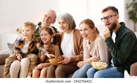 Happy Big Family Enjoying Weekend Together At Home. Grandparents, Mother, Father And Two Little Kids, Sister And Brother, Sitting On Coach And Eating Popcorn While Watching Funny Movie Comedy On TV