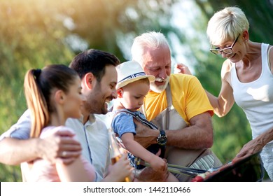 Happy Big Family Gathered Around The Grill At Picnic. Leisure,food,family And Holidays Concept.