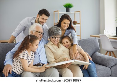 Happy big family grandparents with twin granddaughters and their parents browse the family photo album and share happy memories. Family gathered together in the living room. Family connection concept.