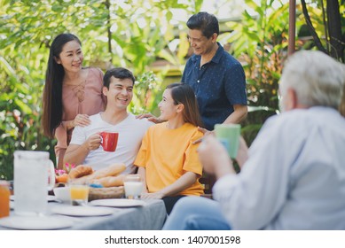 Happy Big Family Have A Lunch At Outdoor In Green Garden. Lunch Or Tea Time On Picnic Table In Summer. Big Family Outdoor Lunch Concept.