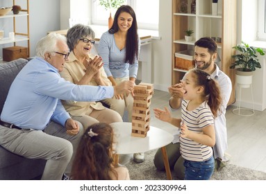 Happy big family with little children enjoying the weekend at home, playing board games and having a good time together. Excited grandkids having fun watching grandpa take a wood block from the tower - Powered by Shutterstock