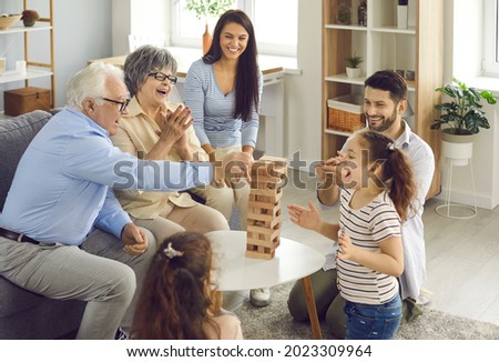 Happy big family with little children enjoying the weekend at home, playing board games and having a good time together. Excited grandkids having fun watching grandpa take a wood block from the tower