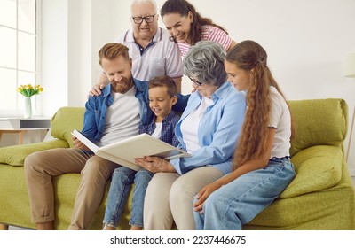 Happy big multigenerational family keep good memories of the past. Cheerful friendly smiling multi generational family sitting on the sofa in the living room and looking through a photo album together - Powered by Shutterstock