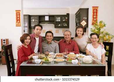 Happy big Vietnamese family having Tet celebration dinner. Scrolls wishing luck and wealth in the background