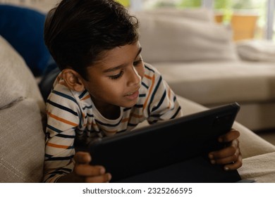 Happy biracial boy lying on couch using tablet in living room. Childhood, free time, technology, communication, entertainment, lifestyle and domestic life unaltered. - Powered by Shutterstock