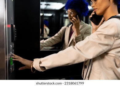 Happy biracial casual businesswoman with blue afro talking on smartphone in office elevator. Casual office, business, communication and work, unaltered. - Powered by Shutterstock