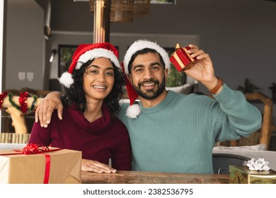 Happy biracial couple with santa hats embracing and smiling among gifts at christmas at home. Togetherness, relationship, christmas, celebration, domestic life, unaltered. - Powered by Shutterstock