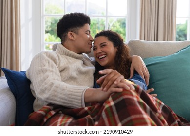 Happy biracial couple sitting on couch under blanket, laughing and embracing in living room. Inclusivity, domestic life, leisure time and togetherness concept. - Powered by Shutterstock