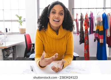 Happy biracial female fashion designer having video call at desk in studio. Fashion, design, creativity, clothing and small business, communication, technology, unaltered. - Powered by Shutterstock