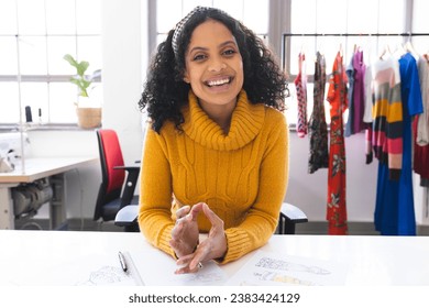 Happy biracial female fashion designer having video call and laughing at desk in studio. Fashion, design, creativity, clothing and small business, communication, technology, unaltered. - Powered by Shutterstock