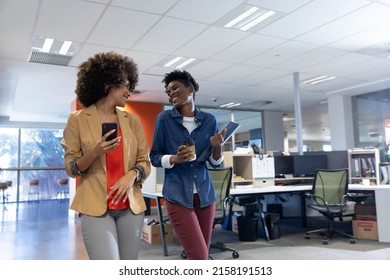 Happy biracial female professionals talking while walking together at modern workplace. unaltered, business team, technology, communication and modern office concept. - Shutterstock ID 2158191513